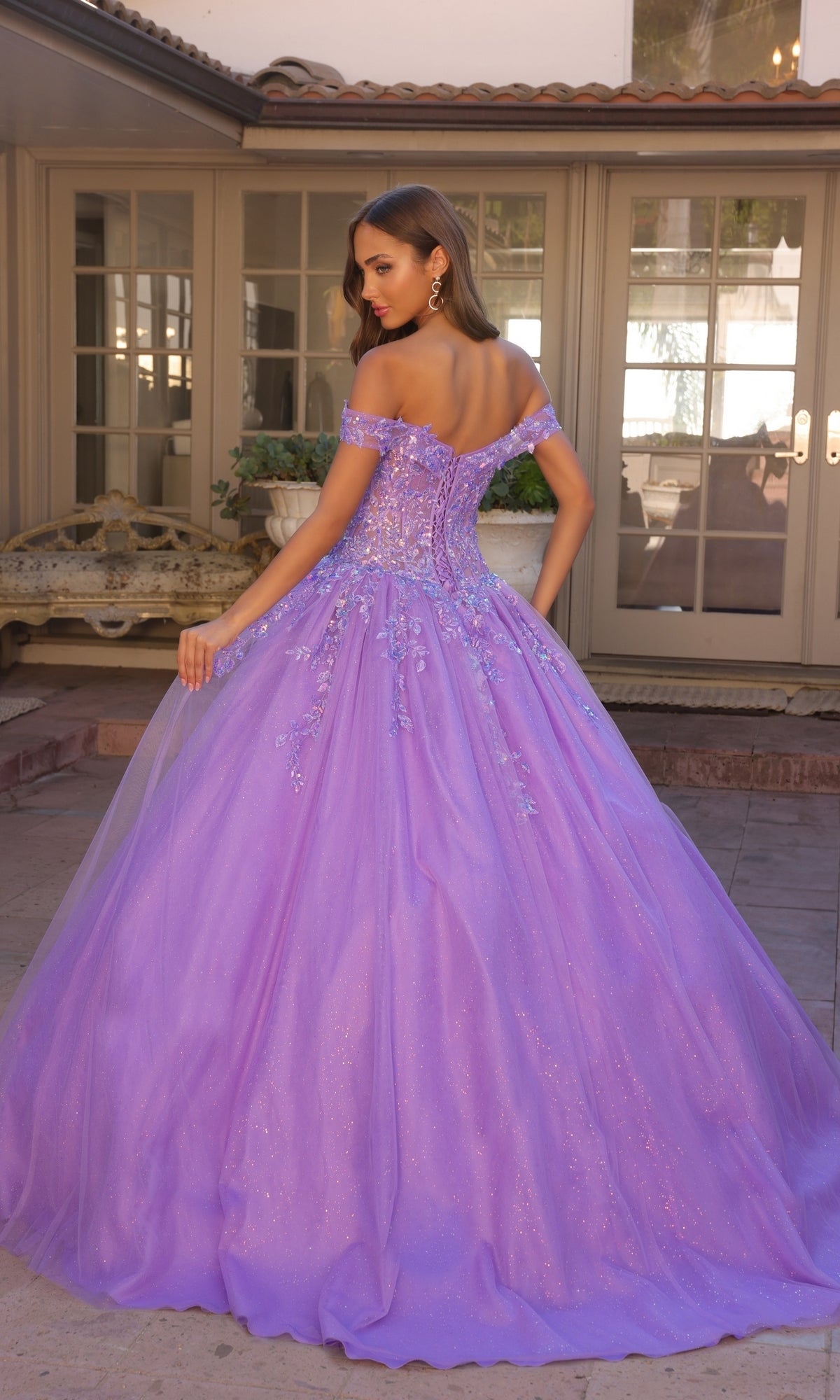 A woman stands outdoors facing away in the Bright Off-the-Shoulder Long Prom Ball Gown H1349, with glass doors and potted plants in the background.